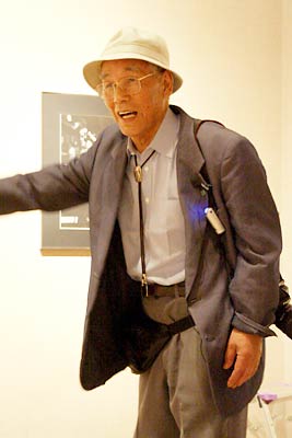 ことし6月6日に燕市産業史料館で開かれた捧武写真展の作品解説会のときの捧さん、肩からカメラを下げて開設する