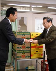寄付したミカンやバナナの入った段ボール箱の前で加藤角利産業社長から国定市長に目録