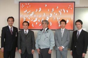 明間印刷所が寄付したトキをモチーフにしたペーパークラフトのアートパネルを背にいちばん左が国定市長、隣りが明間社長