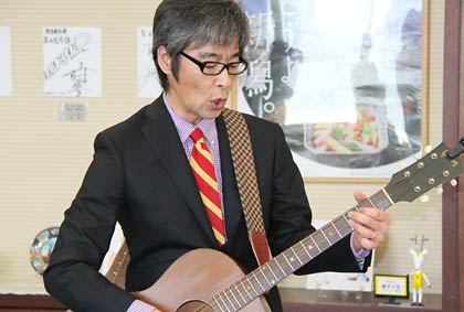 知事室でアコギで「カレーラーメンの歌」を生演奏する矢代さん