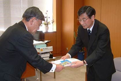 松永教育長(左)に「ポケモンといっしょにおぼえよう!熟語大辞典」を手渡す宮原新聞舗の宮原社長(右)