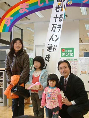 10万人達成の垂れ幕の前で記念撮影