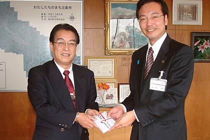 国定市長(右)に100万円の寄付を手渡すコイデエンジニアリングの小出社長(右