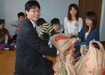 燕市の避難所から初めて市営住宅に入居した姉妹の2世帯6人に鈴木燕市長からコメとポケモンのぬいぐるみを手渡す