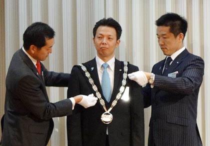 2012年度理事長に決まった五十嵐さん（中央）にプレジデンシャルリーフをかける梨本直前理事長（左）と長谷川2009年度理事長（右）