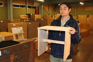 浅野タンスの倉庫市で1日先着8人に3,000円で販売している総桐チェアを手に浅野克也専務