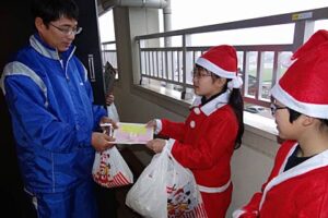 三条市月岡の雇用促進住宅で避難生活を送る人たちにメッセージとともにクリスマスプレゼントの学校田で作ったコメを手渡す三条市立旭小児童