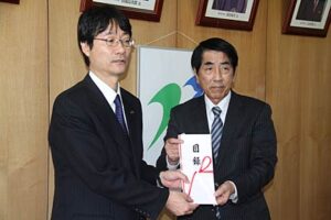 鈴木市長(左)に羽毛欠け布団20枚の目録を手渡す山下家具店の山下社長(右)
