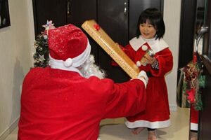 分水商工会青年部のサンタクロースからクリスマスプレゼントを受けとる子どももサンタの衣装でにっこり
