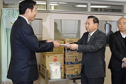「県央寮」管理者の国定市長に切りもちなど寄付の目録を手渡す角利産業の加藤社長