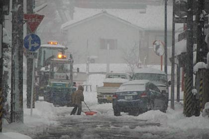 3日午後3時22分、降りしきる雪のなか、三条市興野地内で除雪車が稼働し、市民も雪かき