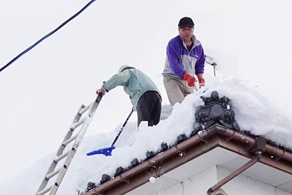 屋根に上がってスコップで雪を落とす