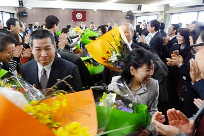 三条市の平成23年度退職者辞令交付式で花束を手に後輩に見送られて会場をあとにする退職者