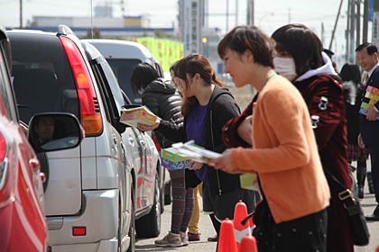 笑顔で先輩ドライバーにティッシュボックや交通安全啓発グッズを手渡す教習生