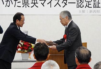 26日開かれた第6回にいがた県央マイスター認定証授与式で岡田県三条地域振興好局長(左)から認定証をうけうるきせる職人の飯塚さん(右)