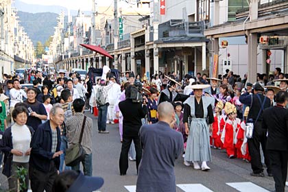酒井さん夫婦を乗せた人力車や稚児の行列が進む商店街大通りは大勢の見物客が見守る