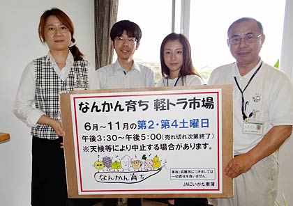 23日にJAにいがた南蒲本店の職員駐車場でスターとする「なんかん育ち　軽トラ市場」のポスターを手に本店職員