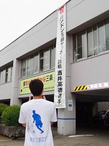 酒井選手のサイン入りTシャツを着て三条庁舎に掲げられた懸垂幕を見る国定市長