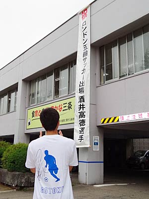 酒井選手のサイン入りTシャツを着て三条庁舎に掲げられた懸垂幕を見る国定市長