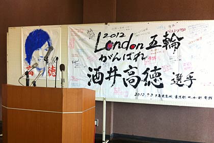  10日の国定三条市長の記者会見で国定市長の背中を飾る高徳選手応援の寄せ書きや高徳選手の顔が描かれたゲーフラ