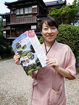 さんじょう和楽会の大竹由香利代表、その後ろは国登録有形文化財に指定された嵐渓荘の木造3階建て「緑風館」