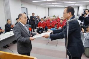 時田勇さん(左)にへら絞り加工（手絞り）マイスターの認定証を手渡す新潟県三条地域振興局の岡田伸夫局長(右)