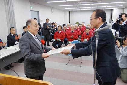 時田勇さん(左)にへら絞り加工（手絞り）マイスターの認定証を手渡す新潟県三条地域振興局の岡田伸夫局長(右)