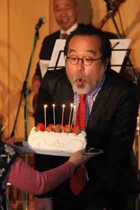 サプライズで中川さんの59回目の誕生日を一足早く祝い、デコレーションケーキのろうそくを吹き消す中川さん