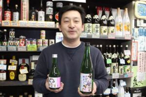 右手に吟醸「きららん」、左手に清酒「分水桜まつり」を持つコメゴ酒店の古沢さん