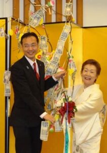 国定市長に善意の下がったまゆ玉飾りを手渡す「スナックマンマ」の五十嵐さん