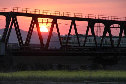  25日の夕焼け空と信濃川の石上大橋上流側に架かる弥彦線鉄橋を渡る電車