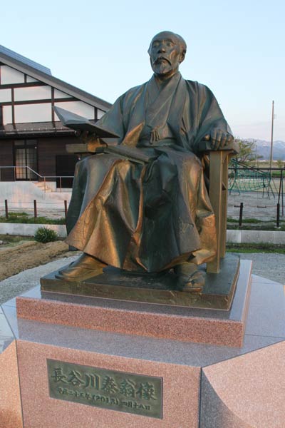 長岡市新組地区の北越戊辰戦争伝承館前に建立された長谷川泰の銅像、左奥に見えるのが伝承館
