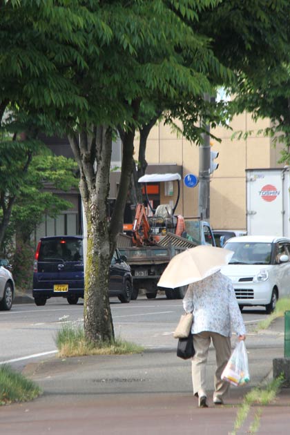28日午後、三条市・旭町通りで買い物袋を下げて日傘を差して歩く