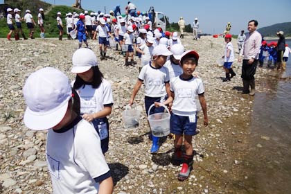 アユの稚魚の入ったバケツを下げて放流に向かう児童