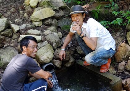 棚田を維持管理する佐野誠五さんの案内でわき水「大久保の清水」を味わう