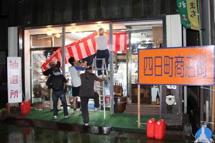  26日夜、四日町商店街の商店主らが「酒のニラサワ」に集まって抽選会場を設営