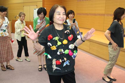 野菜や果物のキャラクターのアクセサリーをたくさんつけた服で来場者の写真撮影に応える砂田さん