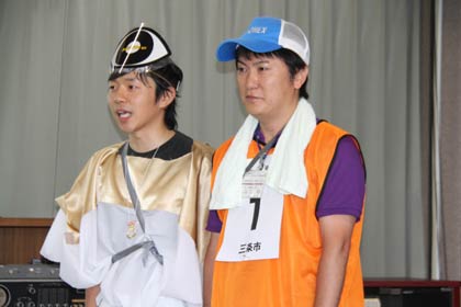 10日の記者会見でゲームを寸劇風に披露した健康づくり課スポーツ振興室職員、左が鬼の「MiiiKe」のふん装、右が参加者の服装