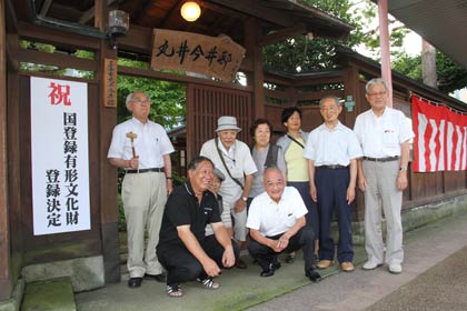 国登録有形文化財への登録が決まった「旧今井家住宅新館」前で、登録決定を知らせる看板を取り付けて記念撮影する三条市丸井今井邸保存会の正副会長や理事