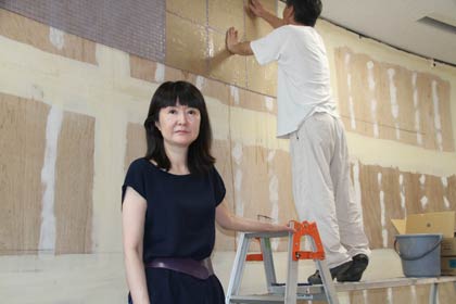 19日、ガラスモザイクの取り付け作業が始まった吉田小学校図書室を訪れた壁画家の松井エイコさん、後ろは壁面にタイルを貼り付けるモザイキストの薄井さん