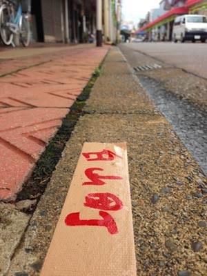 雨で道路にチョークで小間割を書けなかったため、文字を書いたガムテープを歩道に張って対応