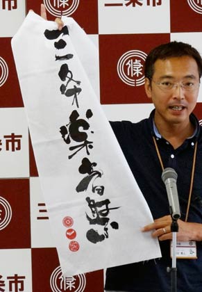 27日開かれた国定三条市長の記者会見で、9月1日の三条楽音祭で販売するオリジナルチャリティ手ぬぐいを紹介する国定市長