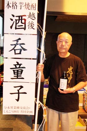  下孝酒店と分水異業種交流会の共同企画の芋焼酎「越後酒呑童子行列」を手に下孝酒店の下村さん