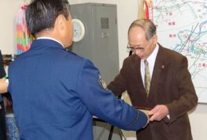 小林三条署長(左)から全国防犯協会連合会の防犯功労章(銅章)の伝達を受ける小林さん