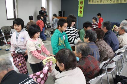 粟生津地区連合老人会に反射シールを張り付けて作ったエコバッグ60個をプレゼントする粟生津小学校2年生