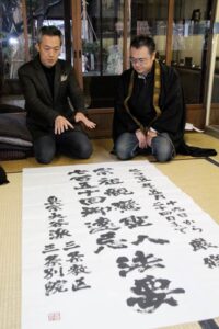 金沢翔子さんが揮毫した宗祖親鸞の七百五十回御遠忌法要を告げる題字を玉川堂に届けた三条教区宗祖親鸞聖人七百五十回御遠忌実行委員会広報部会主査の渡辺さん(右)と玉川堂の玉川社長