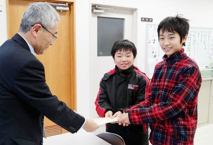 新聞回収などの売り上げ金1,200円を赤い羽根共同募金に寄付してほしいと三条市社会福祉協議会の小林事務局長に手渡す裏館小学校6年生の水口君と鈴木君