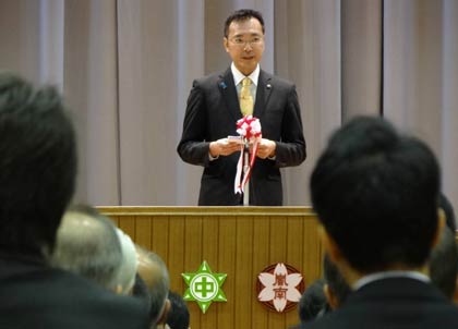 嵐南小と第一中の2つの校章が並ぶ演台を前に式辞を述べる国定市長