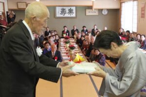 吉田地区老人クラブ連合会の熟年成人式で栗林会長から熟年成人者に記念品贈呈