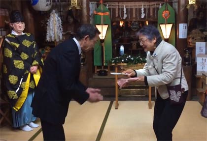 竹井さんから宮町商店街振興組合理事長の鈴木さんに自治会からの激励金を手渡す